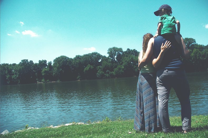 小さな男の子を肩車した父親と寄り添う母親の３人家族が湖を眺めている後ろ姿